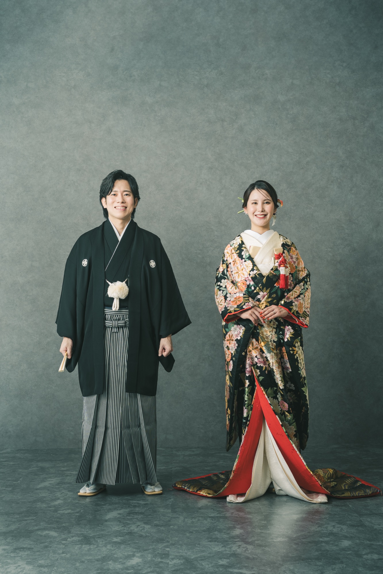 Studio photo of a bride in a red uchikake and the groom in montsuki