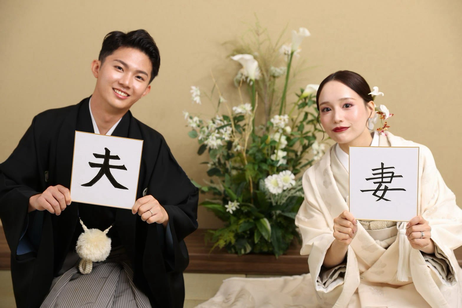 「夫」「妻」の色紙を持つ黒紋付羽織袴の新郎と打掛姿の新婦