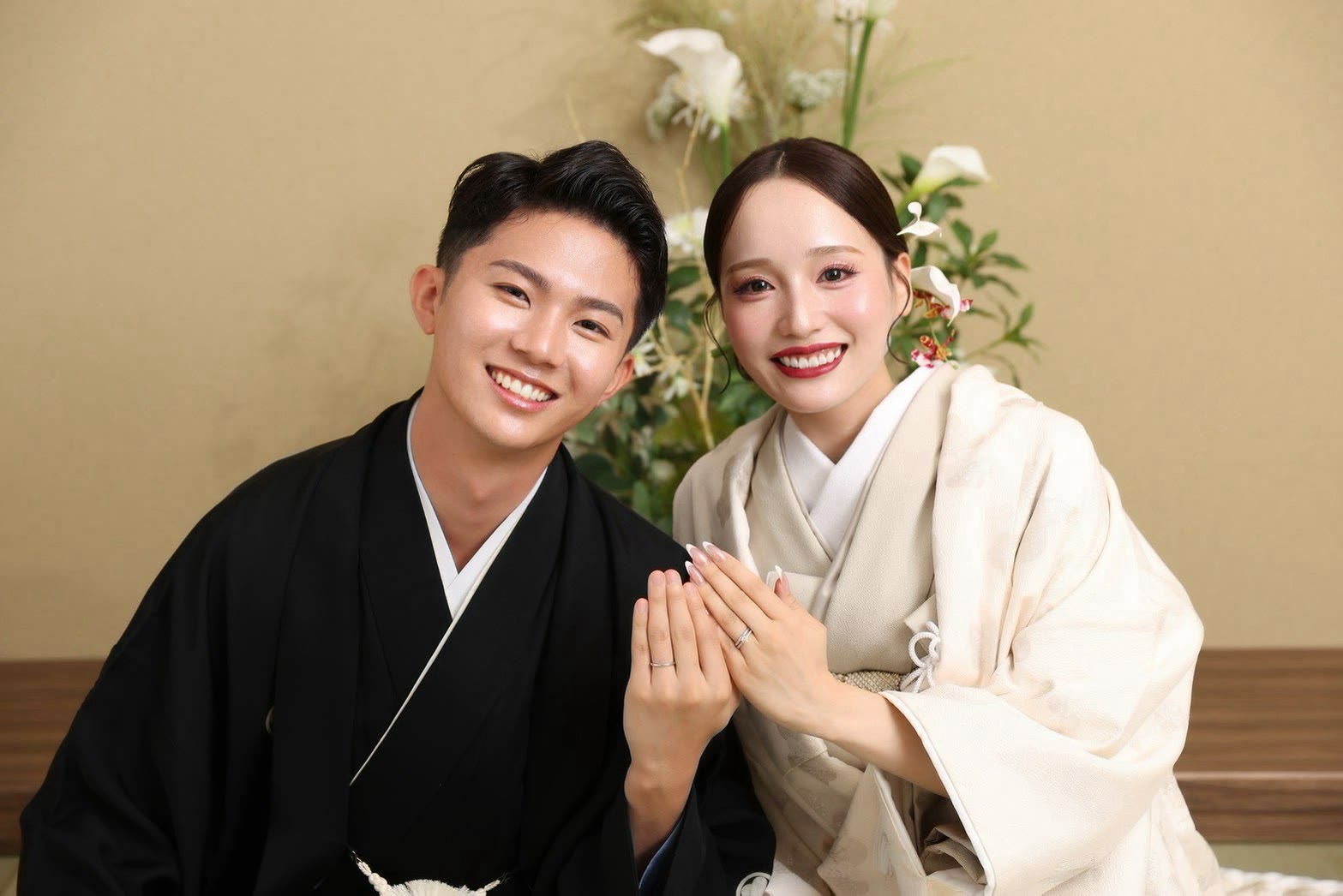 黒紋付の新郎とクリーム色の和装の新婦が手を重ねて結婚指輪を見せるカット